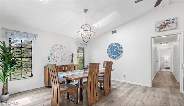 dining space with ceiling fan with notable chandelier, light hardwood / wood-style flooring, and vaulted ceiling with skylight