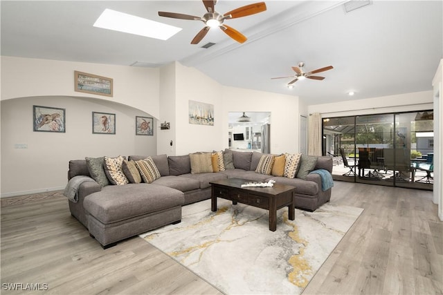 living room with light wood-type flooring, ceiling fan, and vaulted ceiling with skylight