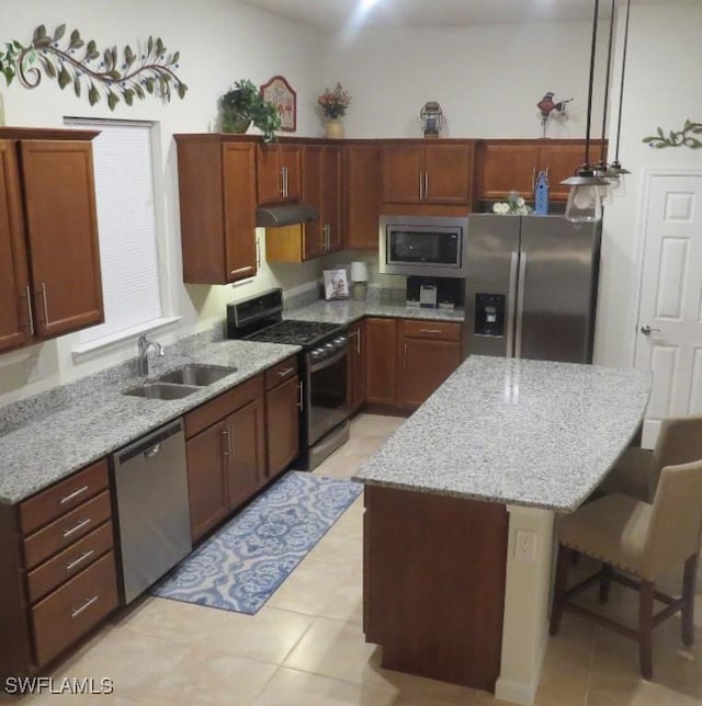 kitchen with pendant lighting, sink, a kitchen breakfast bar, stainless steel appliances, and light stone countertops