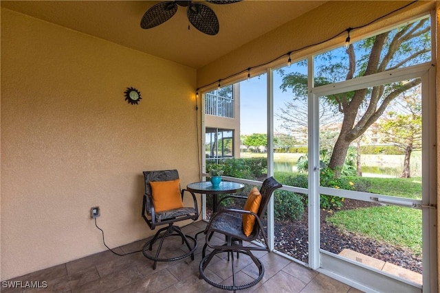 sunroom with ceiling fan and a water view