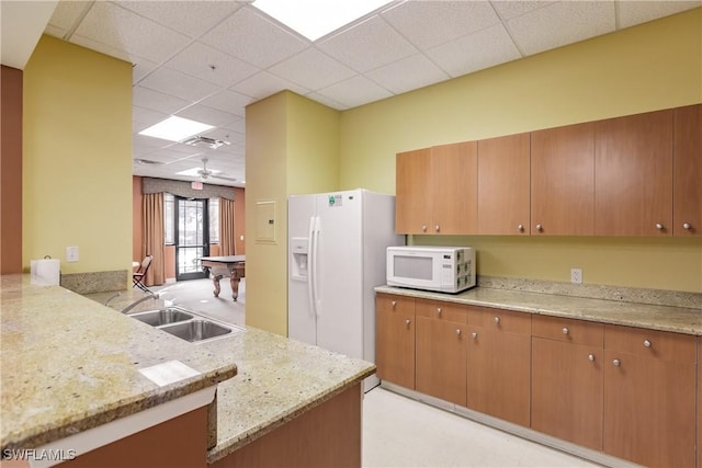 kitchen with sink, a paneled ceiling, kitchen peninsula, white appliances, and light stone countertops