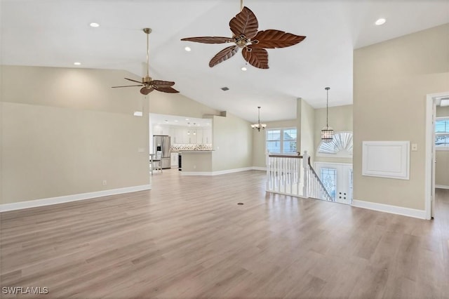 unfurnished living room featuring ceiling fan with notable chandelier, light wood-type flooring, and high vaulted ceiling