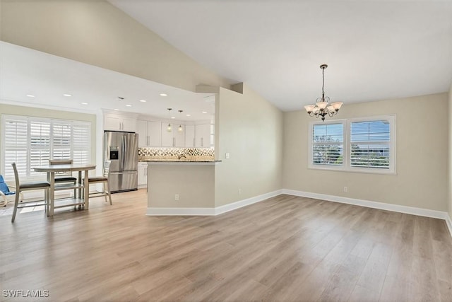 interior space with pendant lighting, stainless steel fridge with ice dispenser, decorative backsplash, a notable chandelier, and white cabinetry