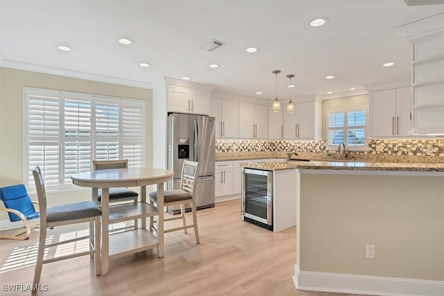 kitchen with light stone countertops, stainless steel fridge with ice dispenser, decorative light fixtures, and white cabinets