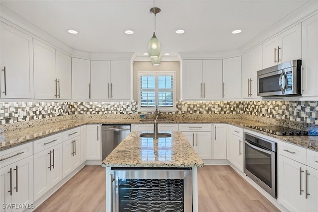 kitchen with hanging light fixtures, stainless steel appliances, wine cooler, light stone counters, and light wood-type flooring