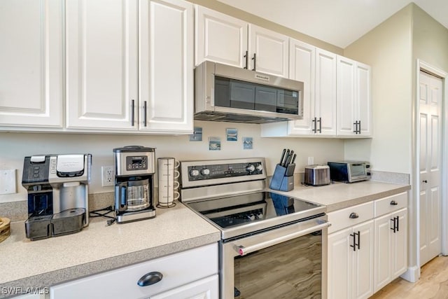 kitchen with stainless steel appliances, white cabinetry, and light hardwood / wood-style flooring