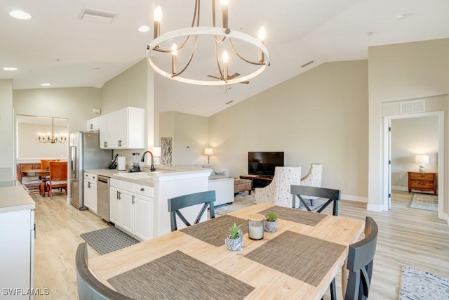 dining room featuring sink, light wood-type flooring, vaulted ceiling, and a notable chandelier