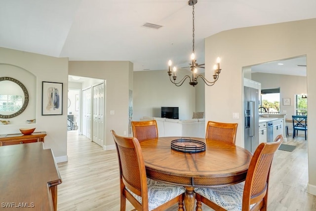 dining space with a notable chandelier, light hardwood / wood-style floors, and vaulted ceiling