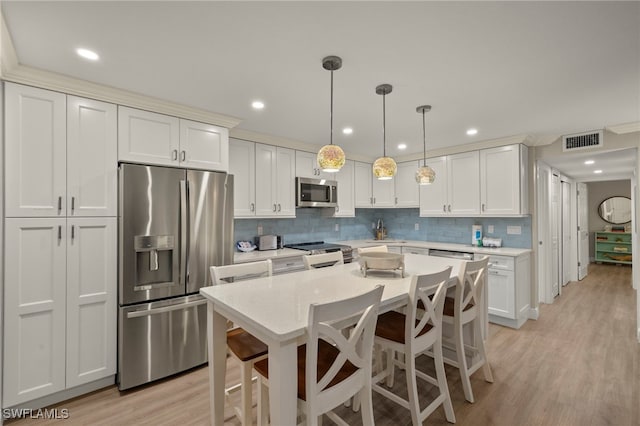 kitchen featuring light wood-type flooring, appliances with stainless steel finishes, white cabinetry, and hanging light fixtures