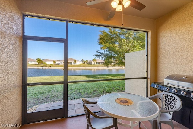 sunroom with ceiling fan and a water view