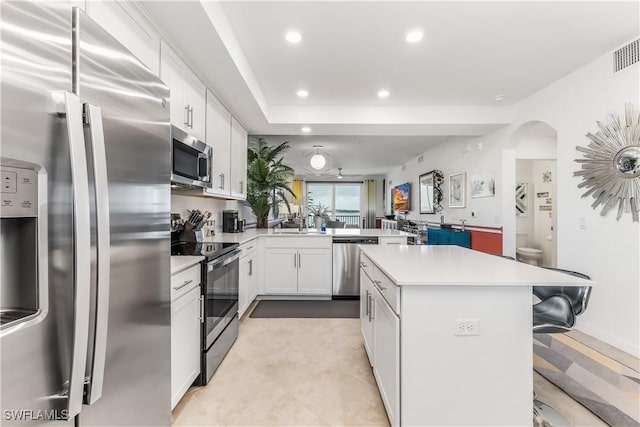 kitchen with white cabinets, a breakfast bar area, a kitchen island, kitchen peninsula, and stainless steel appliances