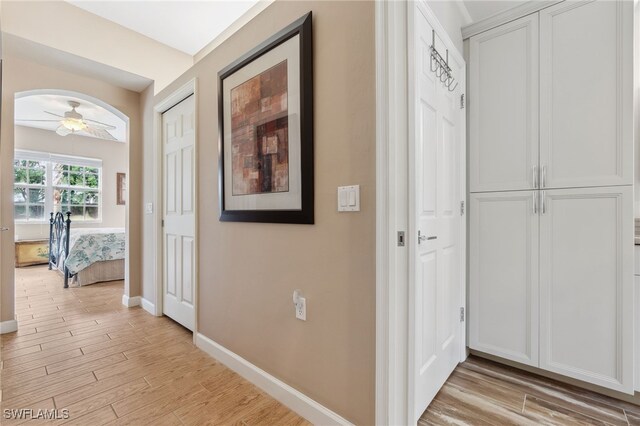 corridor featuring baseboards, arched walkways, and light wood-style flooring