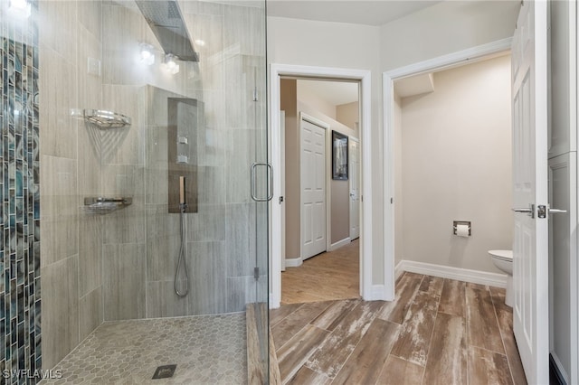 bathroom featuring a shower stall, toilet, wood finished floors, and baseboards