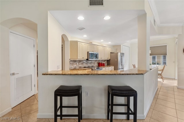 kitchen with backsplash, light stone countertops, appliances with stainless steel finishes, a kitchen bar, and kitchen peninsula