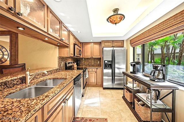 kitchen with stainless steel appliances, stone counters, light tile patterned floors, a tray ceiling, and sink