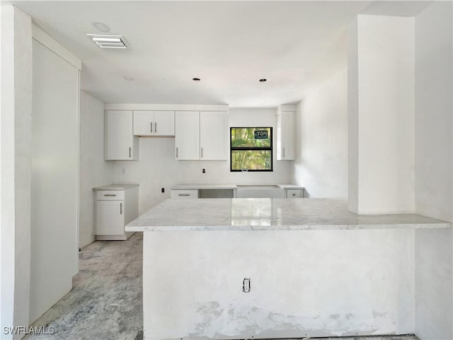 kitchen with kitchen peninsula, light stone countertops, and white cabinets