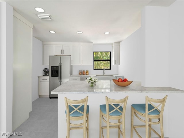 kitchen with white cabinetry, sink, light stone counters, kitchen peninsula, and stainless steel fridge