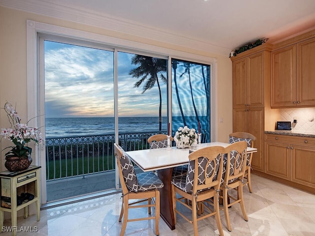 tiled dining space with a view of the beach, a water view, and crown molding