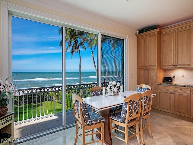 dining area featuring crown molding, light tile patterned floors, a water view, and a view of the beach