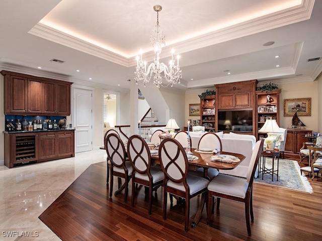 dining area featuring a raised ceiling, wine cooler, light hardwood / wood-style flooring, a notable chandelier, and crown molding