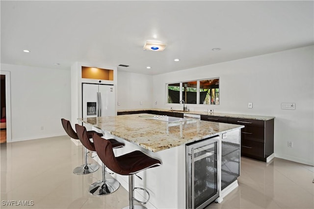 kitchen with refrigerator with ice dispenser, wine cooler, a center island, light tile patterned floors, and dark brown cabinets