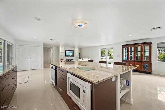 kitchen featuring a kitchen island, white microwave, oven, dark brown cabinetry, and light stone counters