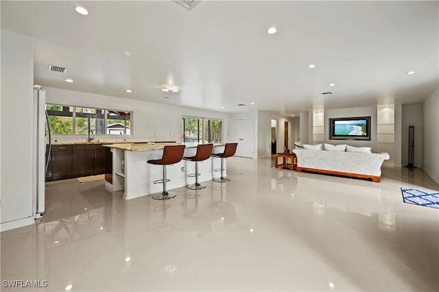 bar featuring stainless steel refrigerator, dark brown cabinets, sink, and light stone counters