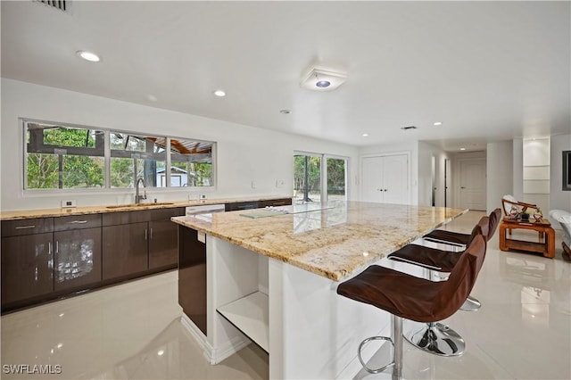 kitchen featuring sink, a breakfast bar, dark brown cabinets, a center island, and light stone countertops