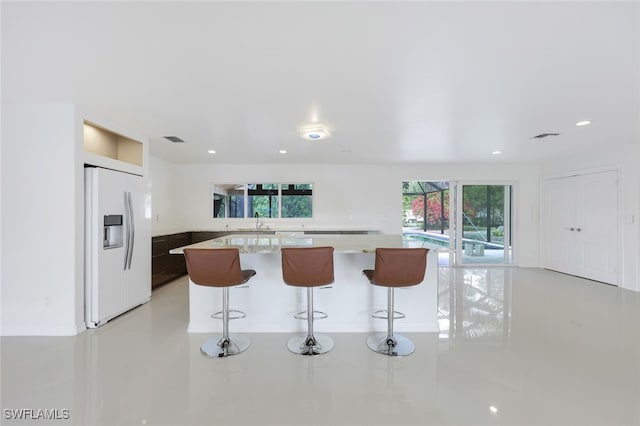 kitchen with sink, light stone countertops, white fridge with ice dispenser, and a breakfast bar