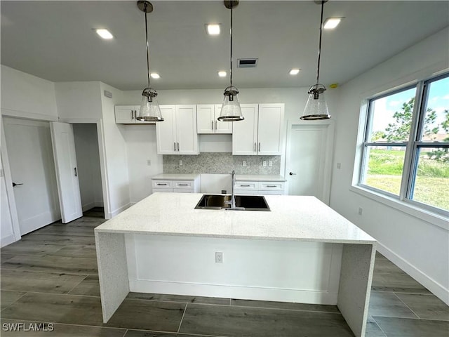 kitchen featuring tasteful backsplash, a kitchen island with sink, sink, and white cabinets