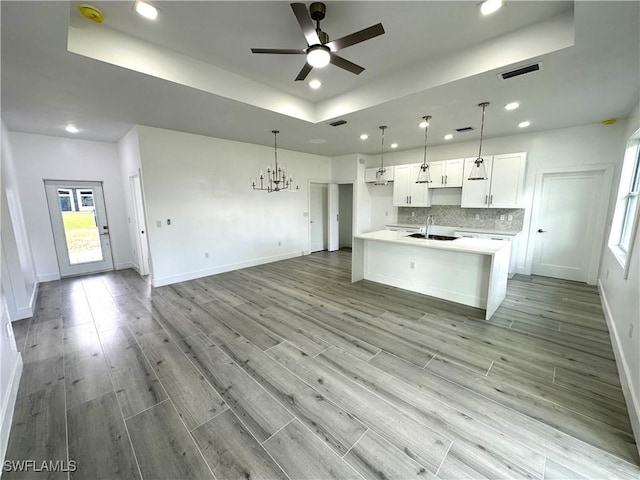 kitchen featuring ceiling fan with notable chandelier, white cabinetry, hanging light fixtures, and a tray ceiling