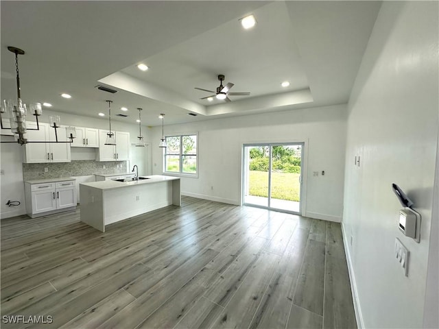 kitchen with pendant lighting, white cabinets, a raised ceiling, light hardwood / wood-style flooring, and an island with sink