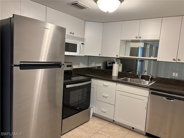 kitchen with appliances with stainless steel finishes, sink, dark stone countertops, white cabinets, and light tile patterned floors