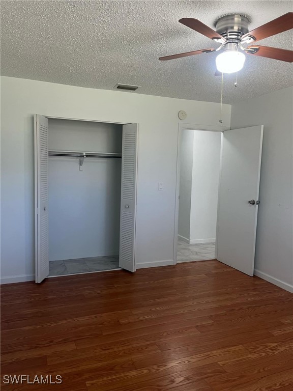 unfurnished bedroom featuring a textured ceiling, dark hardwood / wood-style flooring, a closet, and ceiling fan