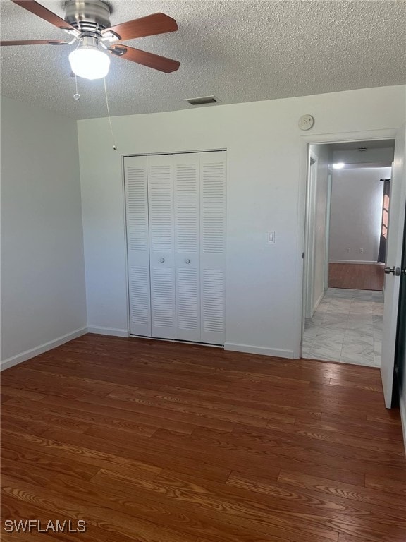 unfurnished bedroom with ceiling fan, a closet, wood-type flooring, and a textured ceiling