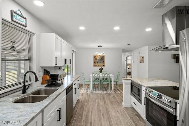 kitchen with sink, wall chimney exhaust hood, light stone counters, white cabinets, and appliances with stainless steel finishes