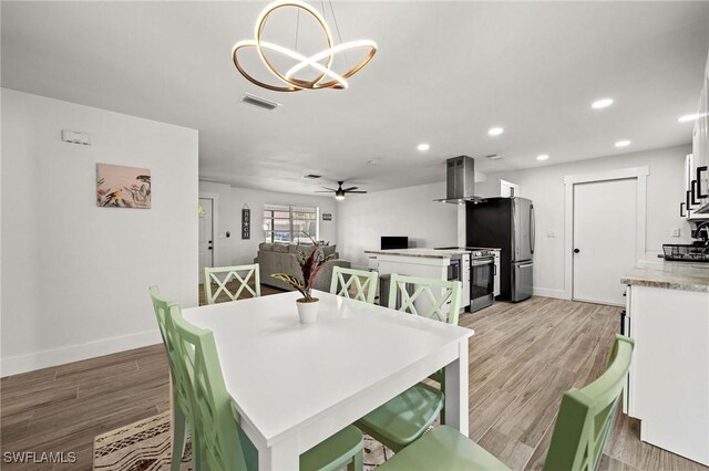 dining area with ceiling fan with notable chandelier and light hardwood / wood-style flooring