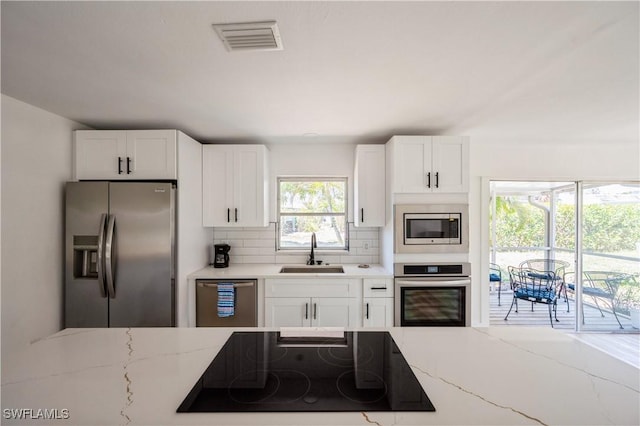 kitchen featuring decorative backsplash, light stone counters, stainless steel appliances, sink, and white cabinets