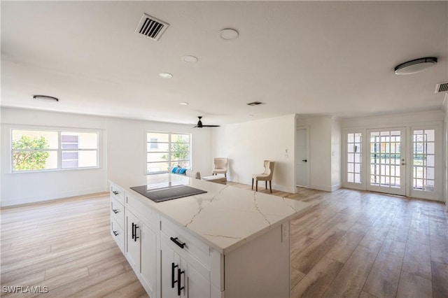 kitchen with light stone countertops, black electric cooktop, white cabinetry, and light hardwood / wood-style flooring