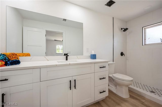 bathroom with a tile shower, vanity, toilet, and hardwood / wood-style floors