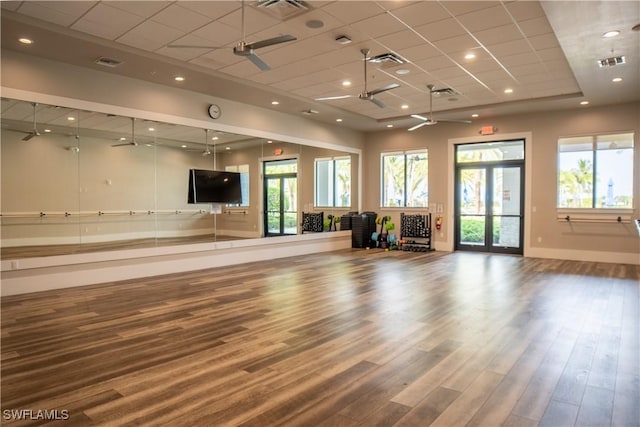 exercise room with ceiling fan, hardwood / wood-style floors, a paneled ceiling, and a healthy amount of sunlight