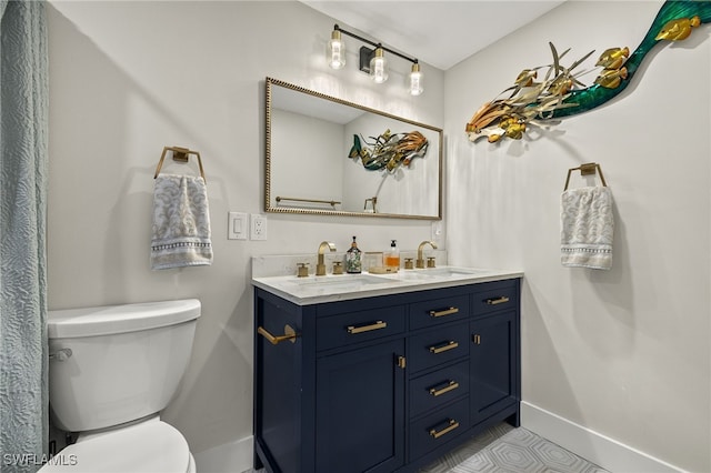 bathroom with toilet, double vanity, baseboards, and a sink