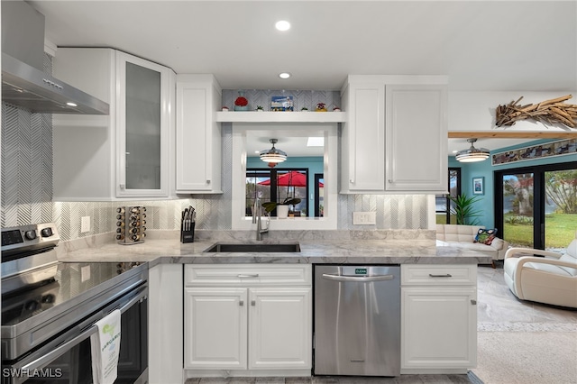 kitchen featuring a sink, white cabinets, appliances with stainless steel finishes, wall chimney exhaust hood, and glass insert cabinets