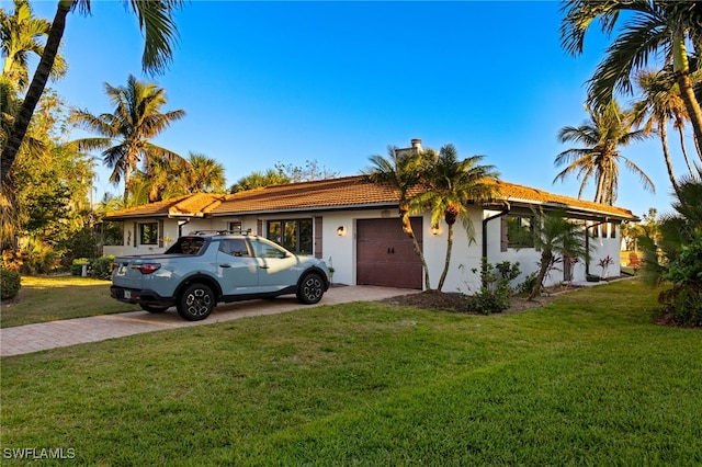 ranch-style home with an attached garage, a front lawn, and decorative driveway