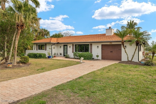 ranch-style home with a chimney, a garage, driveway, a tiled roof, and a front lawn