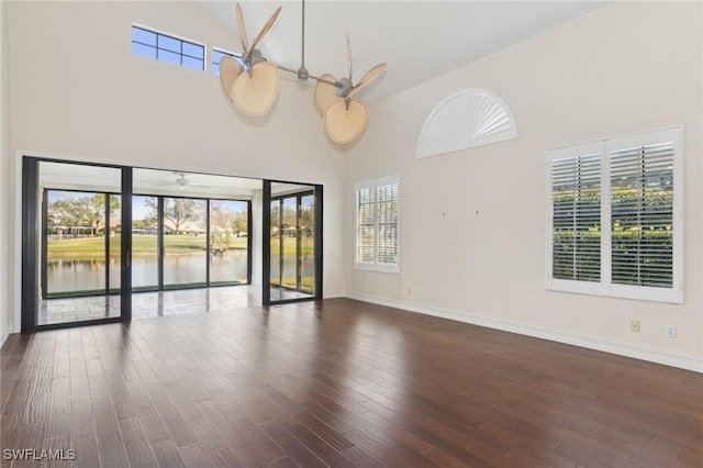 spare room featuring a water view, dark wood-type flooring, and high vaulted ceiling