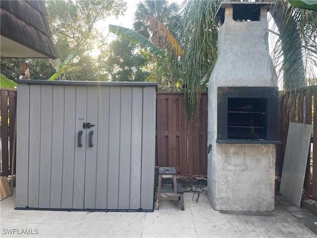 view of outdoor structure with a fireplace and fence