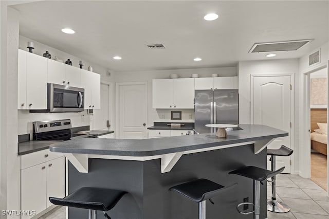 kitchen with white cabinets, a kitchen bar, light tile patterned floors, and stainless steel appliances