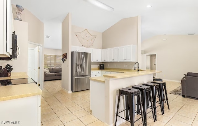 kitchen with white cabinetry, kitchen peninsula, stainless steel fridge, a breakfast bar area, and light tile patterned flooring