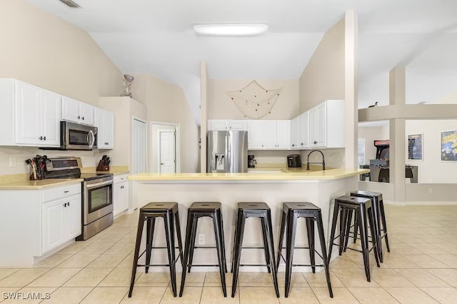 kitchen with white cabinetry, stainless steel appliances, a kitchen breakfast bar, kitchen peninsula, and light tile patterned floors